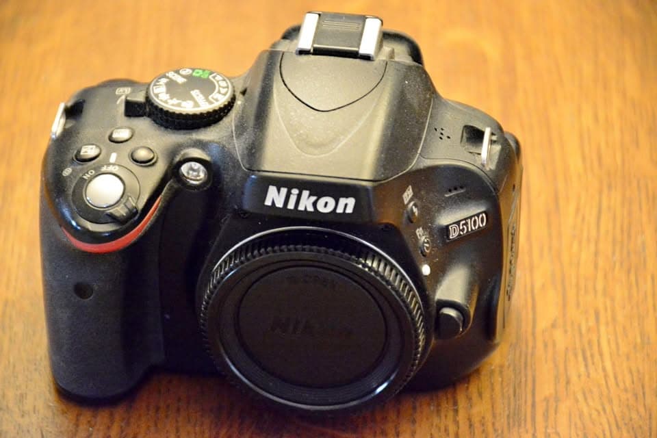 Nikon D5100 DSLR camera body with a body cap, on a wooden table